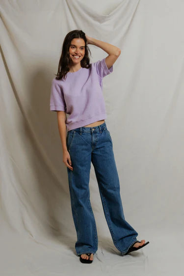 Woman wearing a purple sweater and blue jeans against a plain background