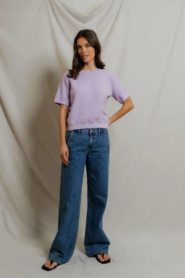 Woman wearing a light purple sweater and blue jeans against a plain background