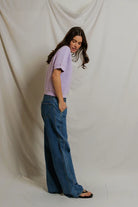 Woman wearing a light purple shirt and blue jeans against a plain background