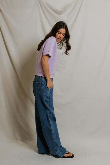 Woman wearing a light purple shirt and blue jeans against a plain background