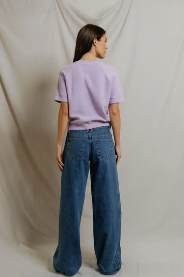 Person wearing a light purple t-shirt and blue jeans against a plain background