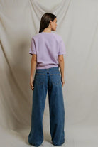 Person wearing a light purple t-shirt and blue jeans against a plain background