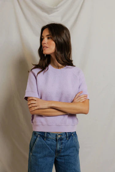 Woman wearing a light purple sweater and blue jeans against a plain background