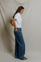 Woman wearing a white t-shirt and blue jeans against a plain background