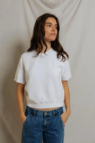 Woman wearing a white crop top and blue jeans against a plain background