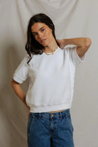Woman wearing a white sweater and blue jeans against a plain background