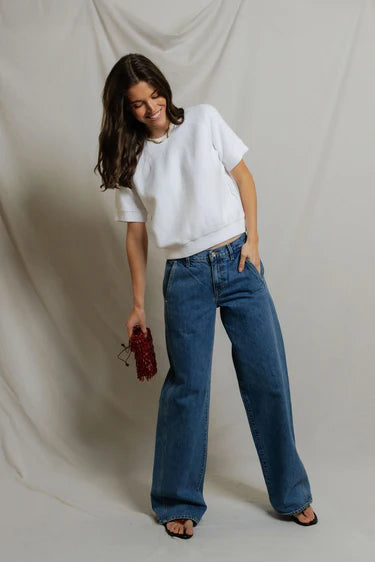 Woman wearing a white t-shirt and blue jeans against a plain background