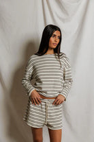 Woman wearing a striped long-sleeve top and shorts against a plain background