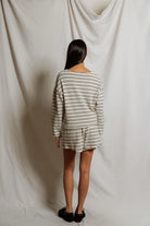 Person wearing a striped outfit standing against a plain white curtain