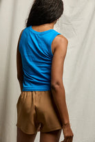 Person wearing a blue sleeveless top and brown shorts against a plain background
