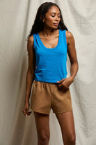 Woman wearing a blue tank top and brown shorts against a plain background