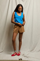 Woman wearing a blue tank top and brown shorts with red sneakers against a plain background