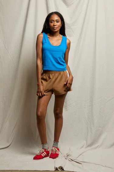 Woman wearing a blue tank top and brown shorts standing against a plain background