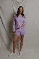Woman wearing a purple outfit standing against a plain background