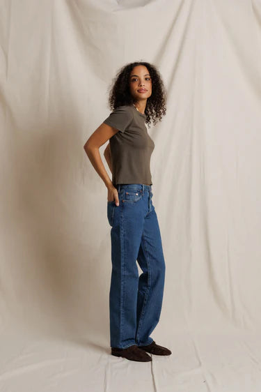Woman wearing a green t-shirt and blue jeans standing against a plain background
