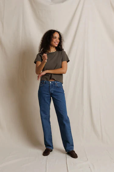 Woman wearing a green t-shirt and blue jeans standing against a plain background