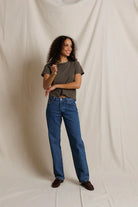 Woman wearing a green t-shirt and blue jeans standing against a plain background