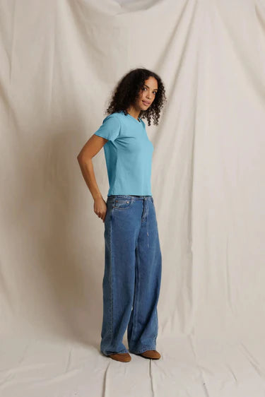 Person wearing a blue t-shirt and jeans standing against a plain white background