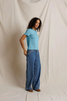 Person wearing a blue t-shirt and jeans standing against a plain white background