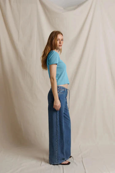 Woman wearing a blue top and jeans standing against a plain background