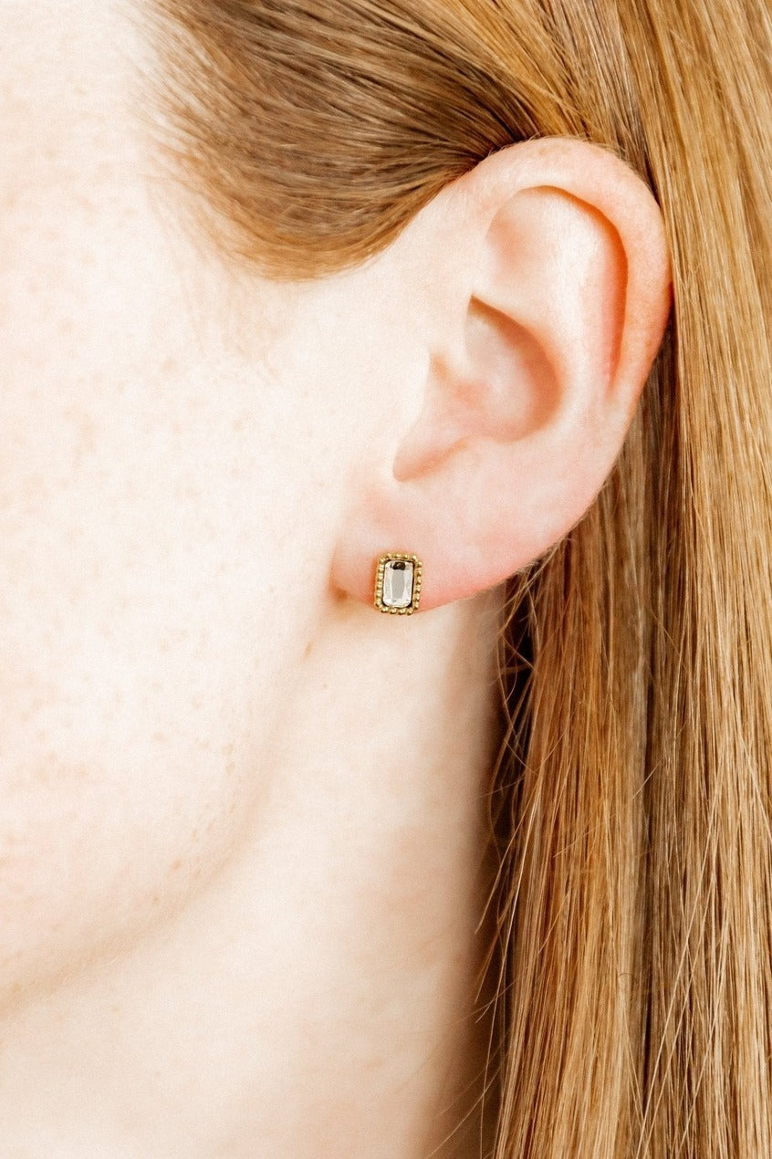 Close-up of an ear wearing a gold earring with a clear gemstone.