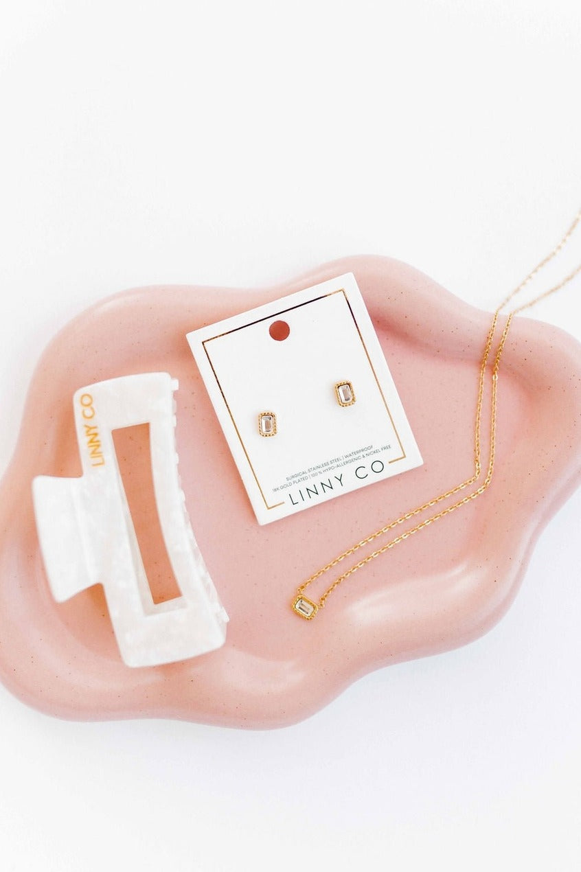 Gold necklace and earrings on a pink stand with LINNY CO packaging.