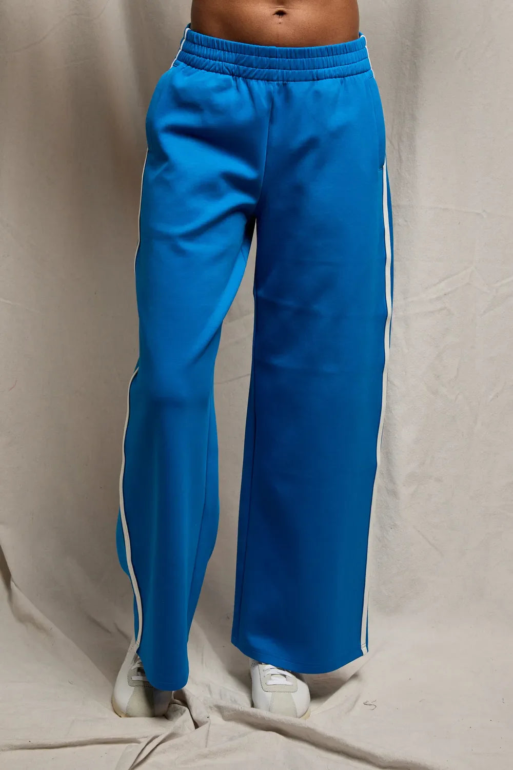 Blue track pants with white stripes on a beige background