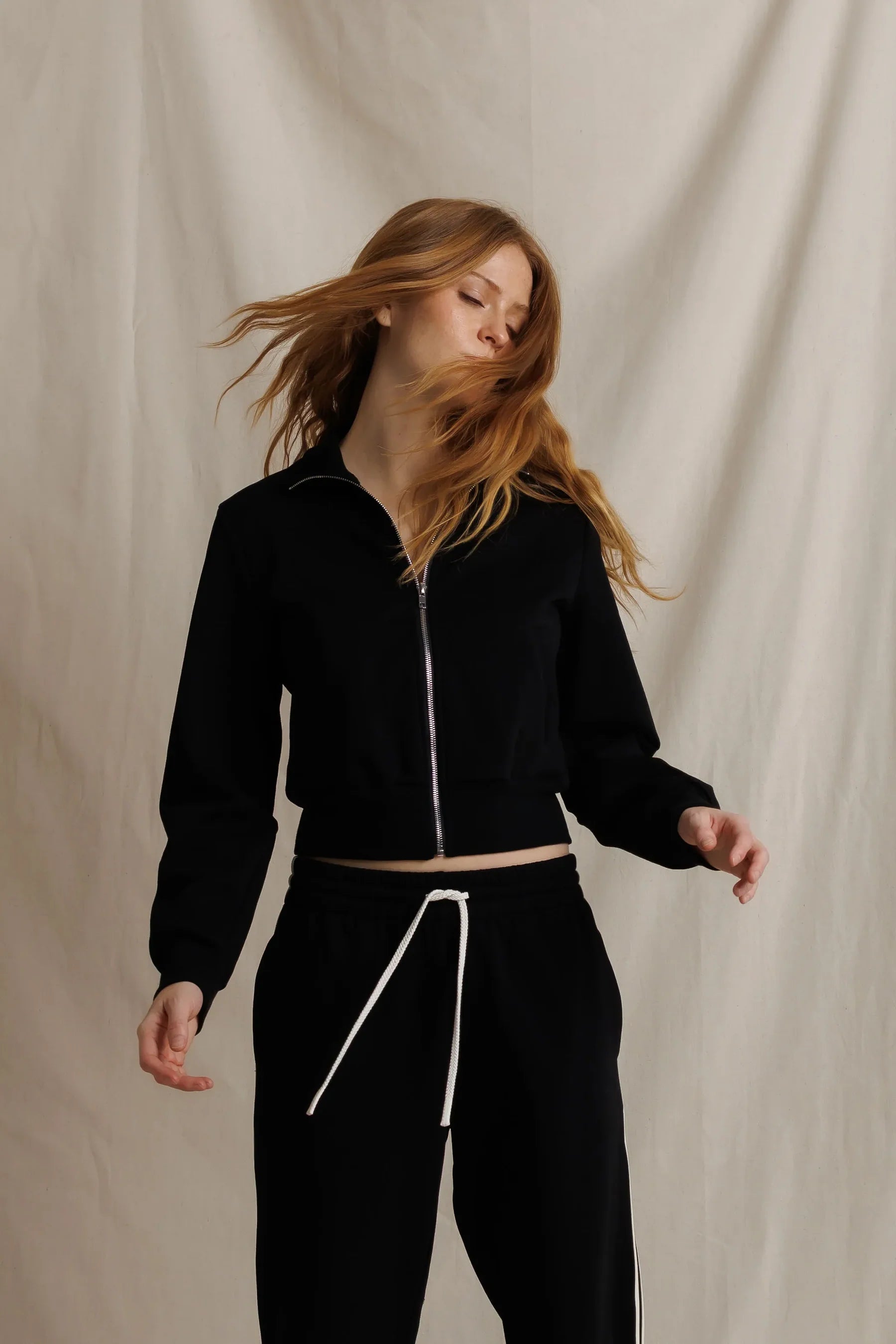 Woman wearing a black tracksuit against a beige background