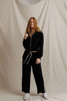 Woman wearing a black tracksuit against a beige background