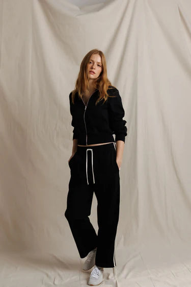 Person wearing a black tracksuit with white drawstrings against a beige backdrop