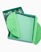 Green fabric item in a box with a floral pattern on a white background