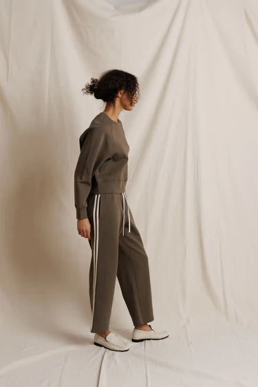 Person wearing a brown tracksuit with white stripes on a plain background