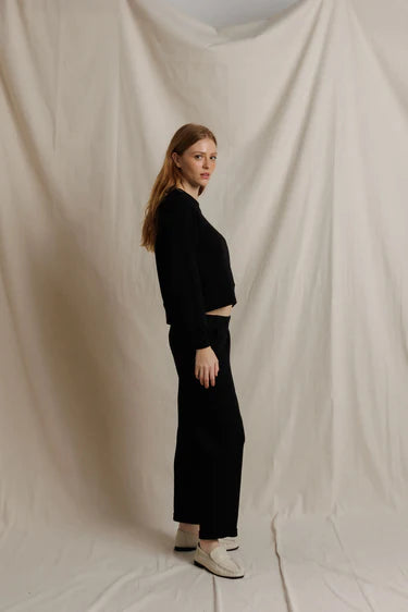 Person wearing a black outfit standing against a beige backdrop