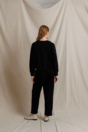 Person wearing a black outfit standing against a plain beige background
