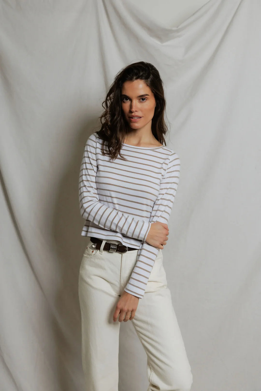 Woman wearing a striped long-sleeve shirt and white pants against a plain background