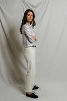 Woman wearing a striped shirt and white pants against a plain background