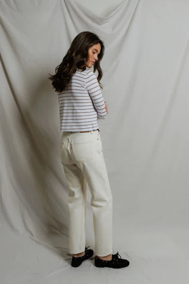 Woman wearing a striped shirt and white pants against a plain background