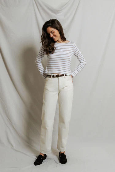 Woman wearing a striped shirt and white pants against a plain background