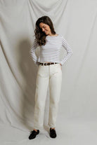 Woman wearing a striped shirt and white pants against a plain background