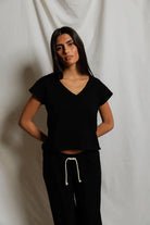 Woman wearing a black top and black pants with a white drawstring against a plain background