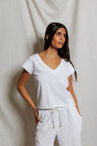 Woman wearing a white top and pants against a plain background