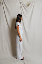 Woman in a white outfit standing against a plain white curtain