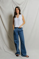 Woman wearing a white sleeveless top and blue jeans against a plain background