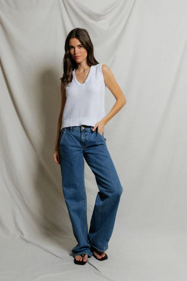Woman wearing a white sleeveless top and blue jeans against a plain background