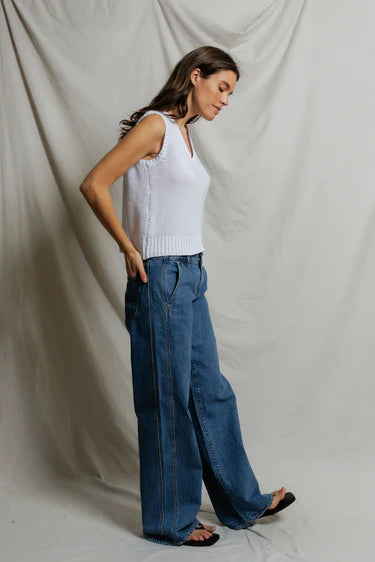 Woman wearing a white sleeveless top and blue jeans against a plain background