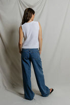 Person wearing a white sleeveless sweater and blue jeans against a plain background
