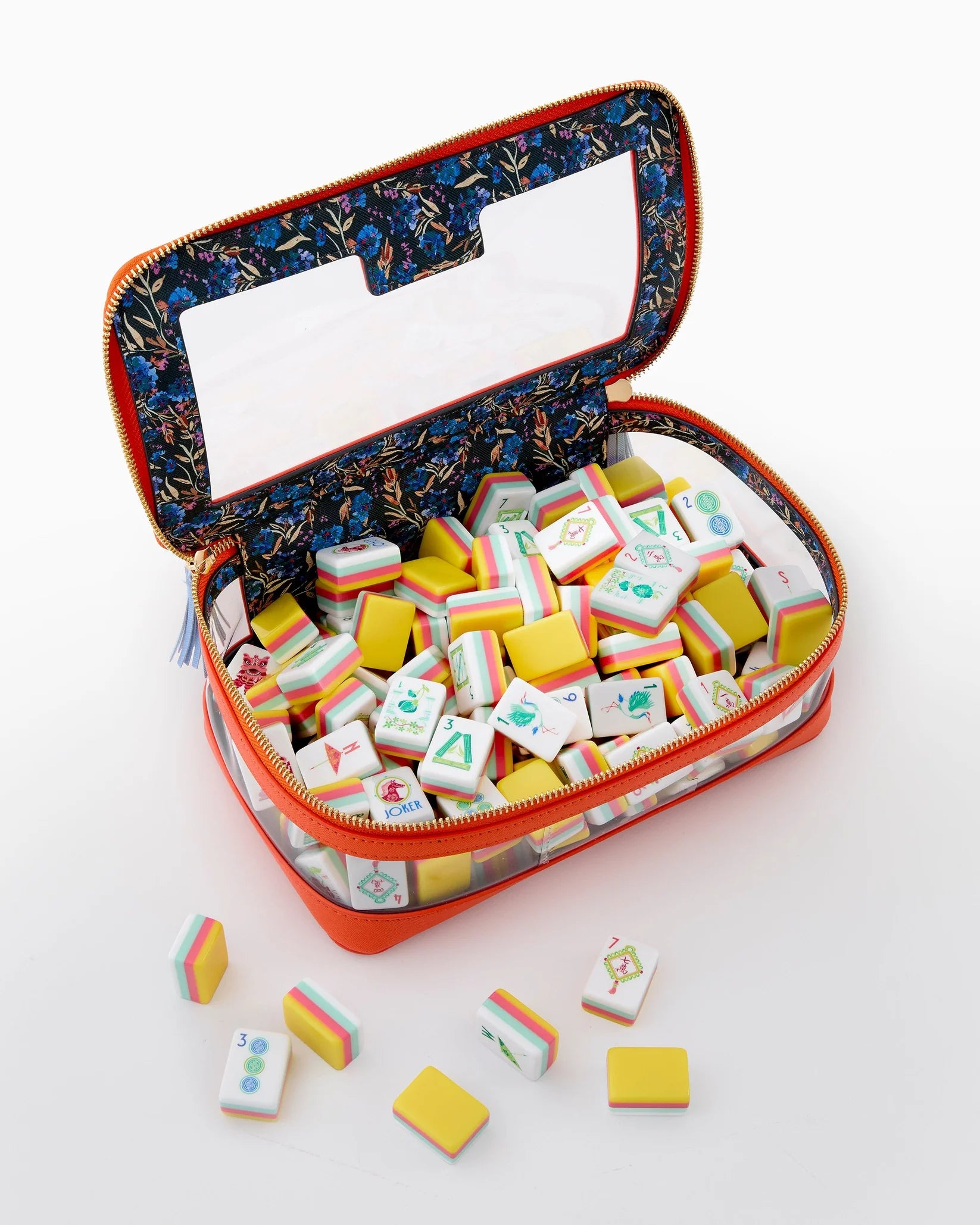 An open zippered carrying case filled with Mahjong tiles, shown on a clean white background. The case has a bright orange-red exterior, a patterned navy blue interior lining, and a clear window on the lid.