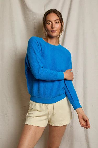 Woman wearing a blue sweater and beige shorts against a neutral background