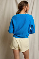Person wearing a blue sweater and light yellow shorts against a plain background