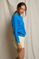 Woman wearing a blue sweater and beige shorts against a plain background